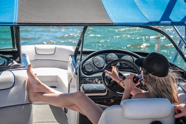 A woman driving a boat with one hand and a drink in her other hand